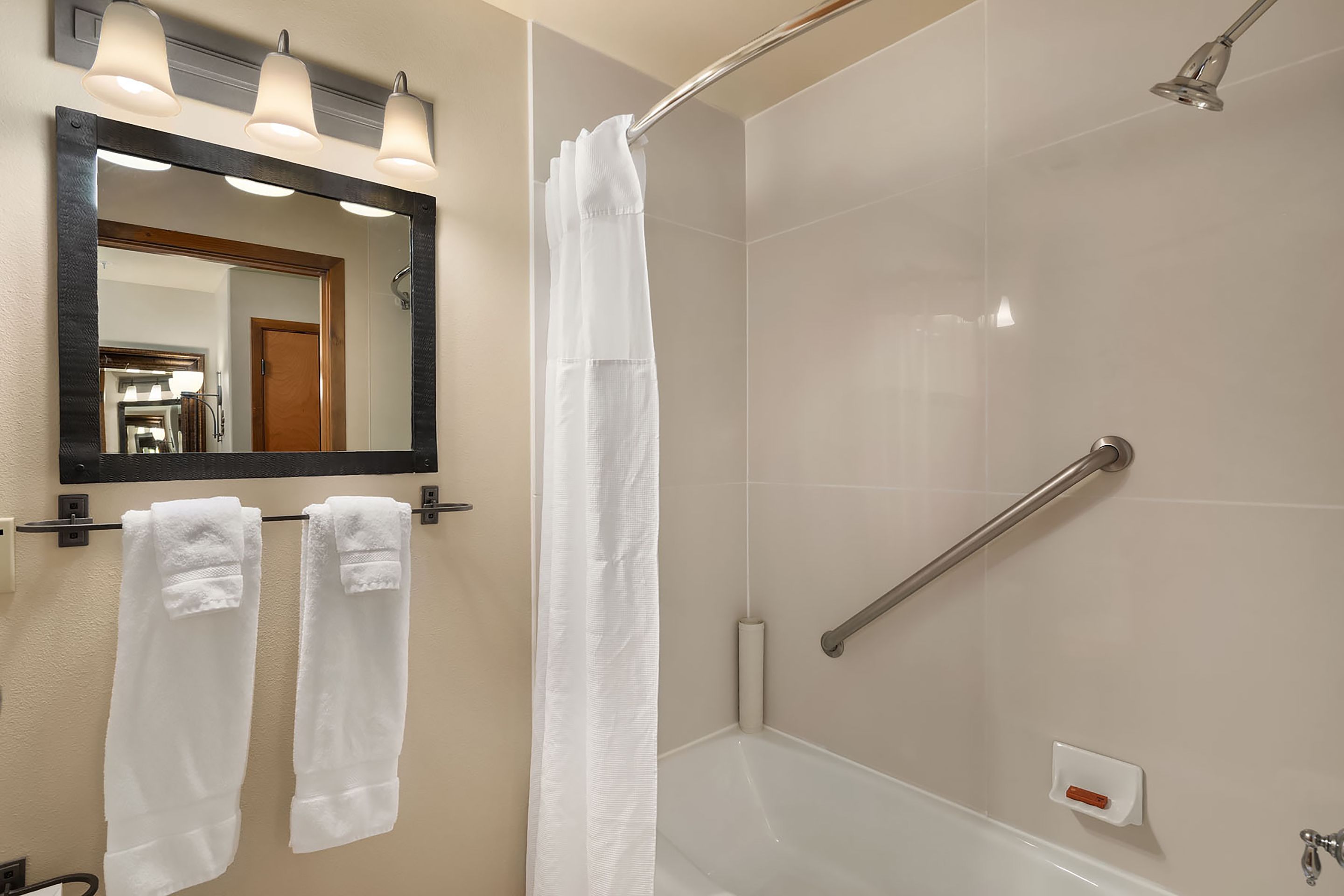 A bathroom with a shower, a mirror, and two towels hanging on a rack.