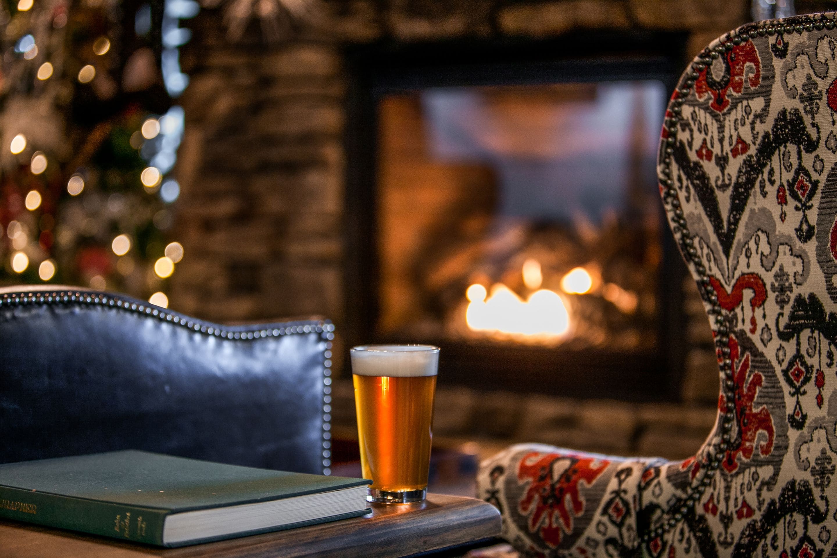 Ein Bierglas auf einem Tisch mit einem Buch und einem gemusterten Sessel.