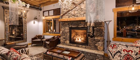 A cozy living room with a stone fireplace, leather furniture, and a chandelier.