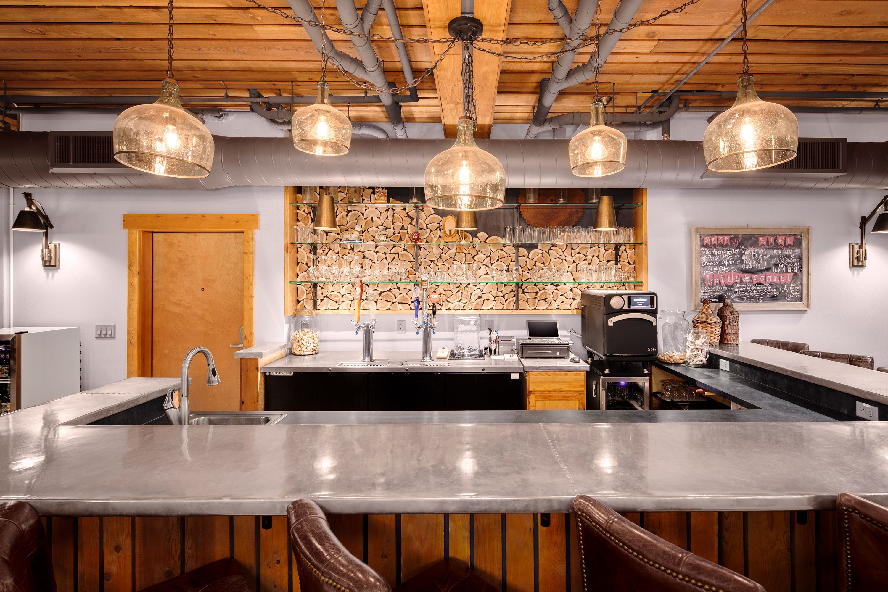 A bar area with a large central counter, wooden ceiling, and hanging pendant lights.
