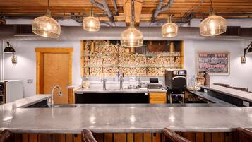 A bar area with a large central counter, wooden ceiling, and hanging pendant lights.