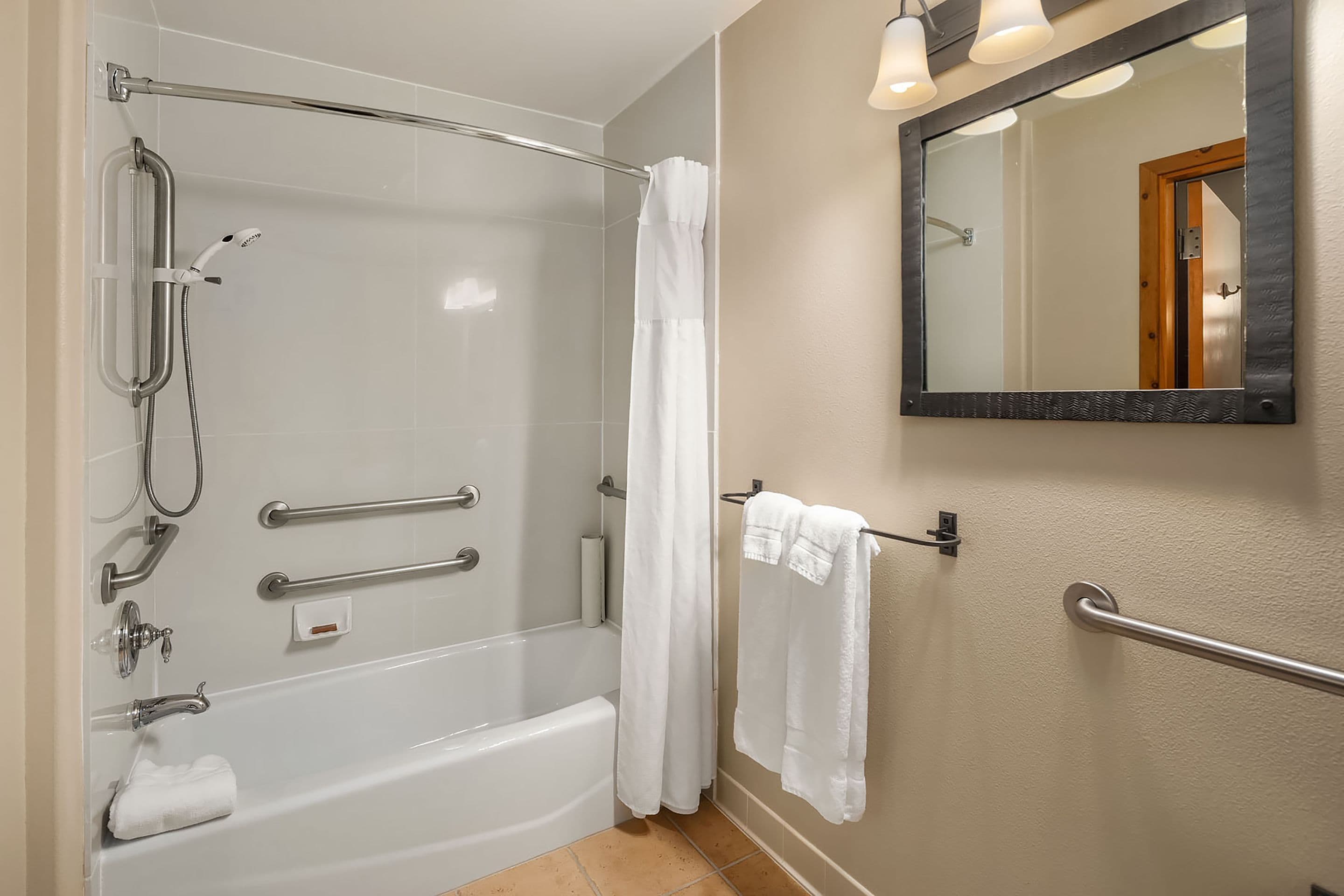 A bathroom with a bathtub, shower, and handrails.
