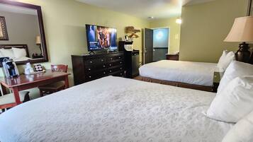 A hotel room with two beds, a desk, a chair, a television, a mirror, and a lamp.