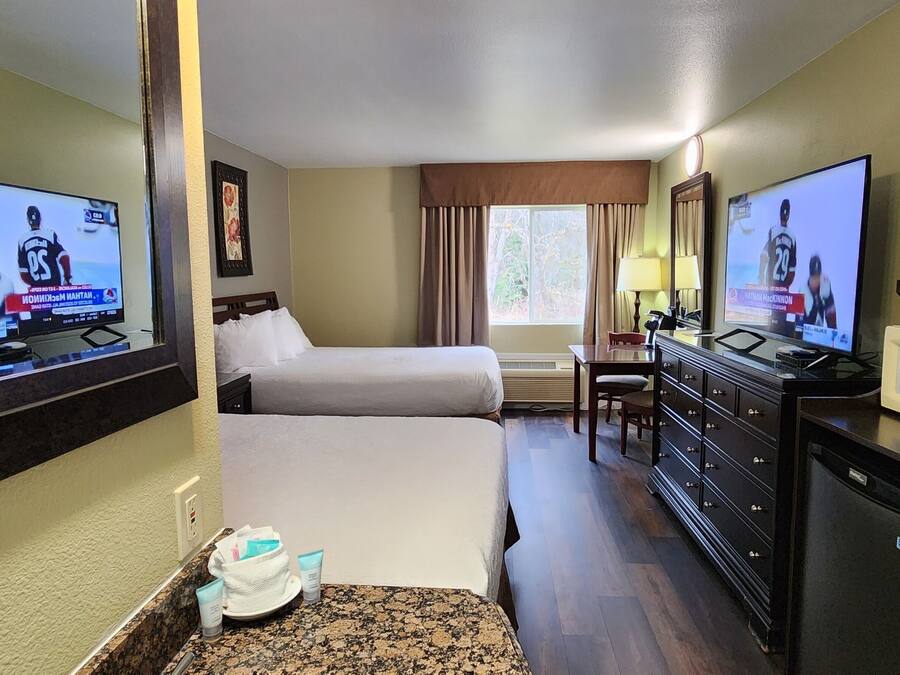 A hotel room with two beds, a television, a desk, a dresser, and a microwave.