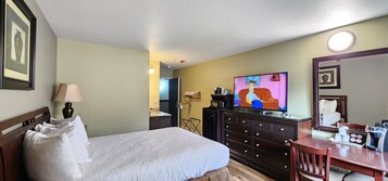 Habitación de hotel con cama, televisión, cómoda, escritorio y espejo.