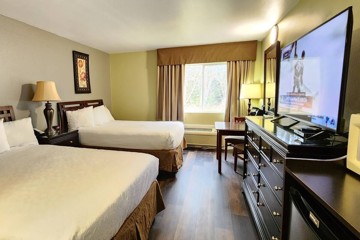 A hotel room with two beds, a TV, a desk, and a dresser.