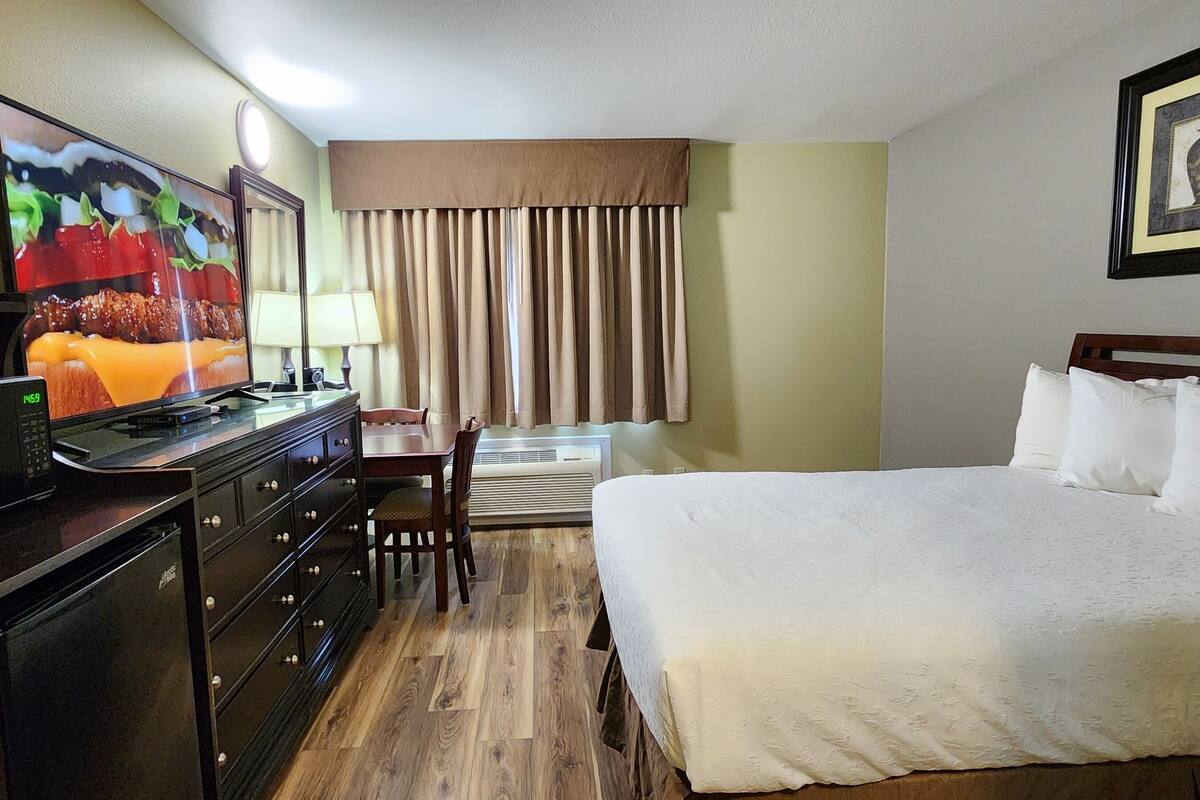 A hotel room with a bed, a TV, a desk with a microwave, and a chair.