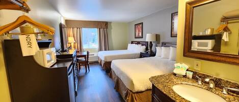 A hotel room with a bed, a desk with a computer, a microwave, a sink, and a mirror.