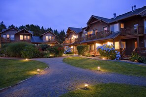 A row of wooden cabins with balconies, a gravel driveway, and well-maintained gardens.