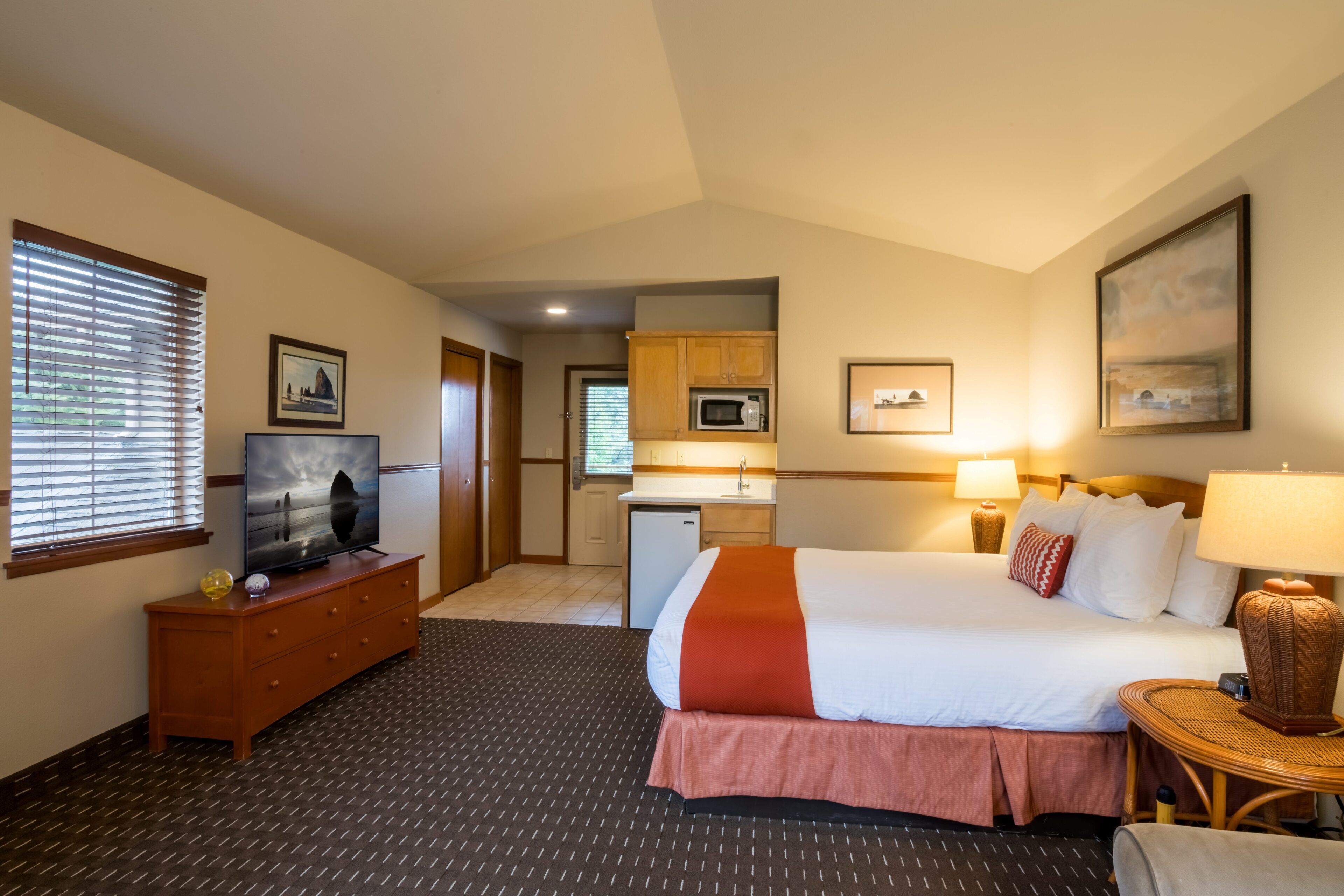 Quarto de hotel com cama, televisão, cozinha compacta e banheiro.