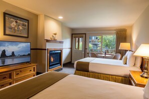 A hotel room with a fireplace, a television, a bed, a desk, and a window with a view of the outside. - Inn at Cannon Beach (Cannon Beach)