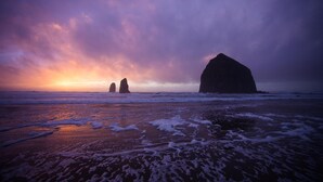 Una playa con grandes formaciones rocosas y olas al atardecer.