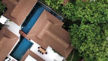Vista aérea de una casa con piscina, un patio con mesa y sillas, y un jardín con árboles.