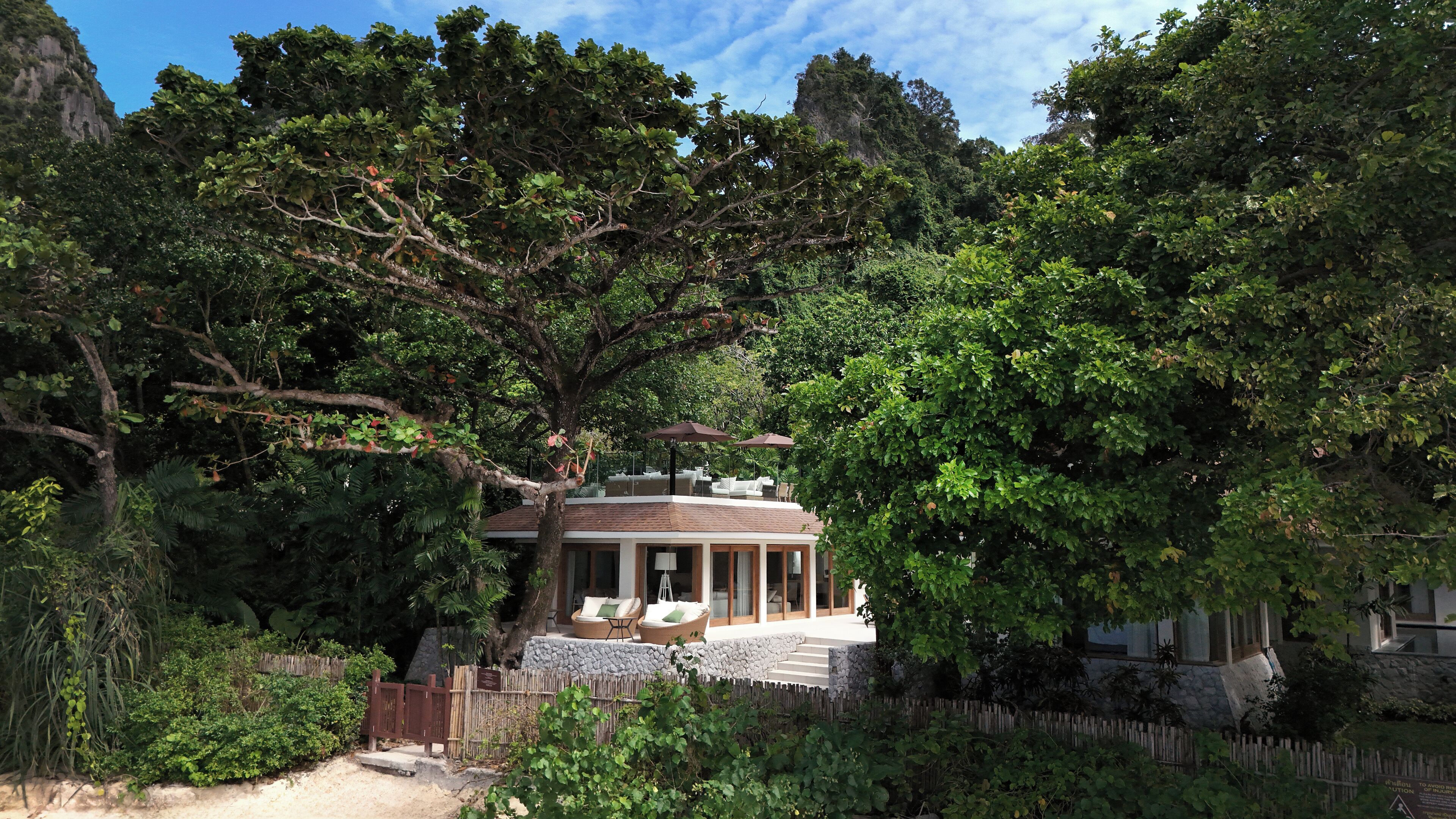 A secluded house surrounded by dense trees and a stone wall.