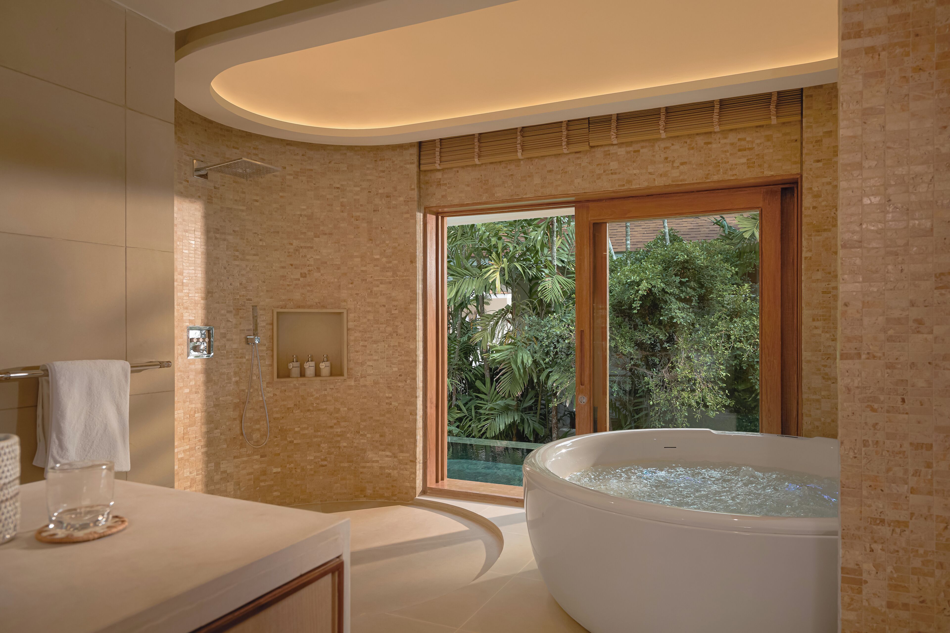 Ein modernes Badezimmer mit einer großen Badewanne, einer gläsernen Dusche und Blick auf üppiges Grün durch ein großes Fenster.