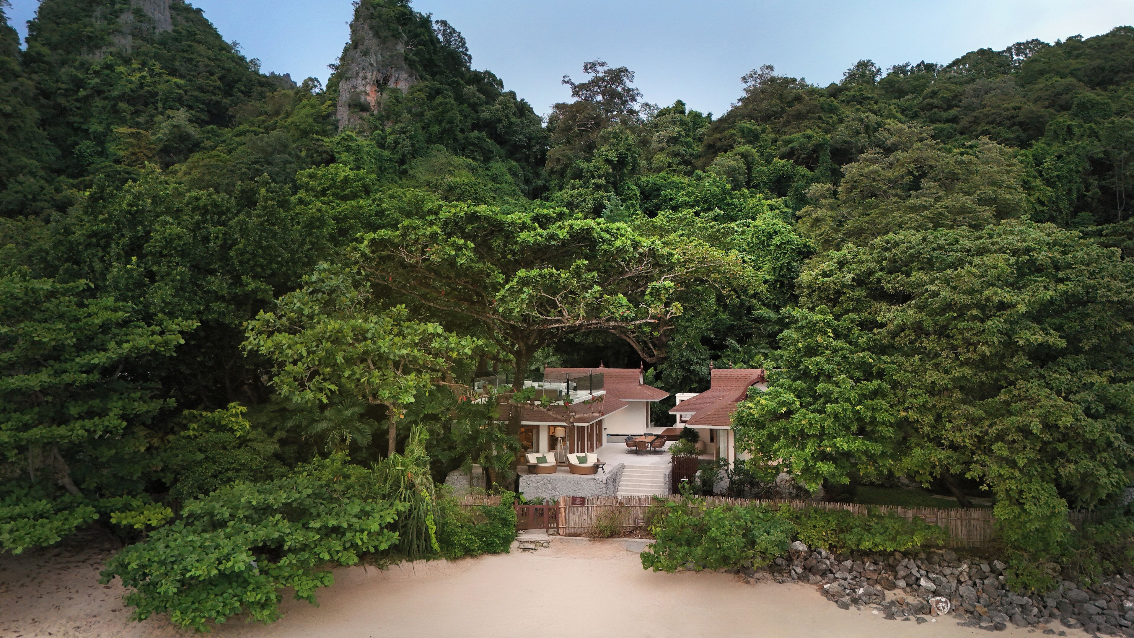 A house surrounded by dense forest, with a sandy path leading to the entrance.