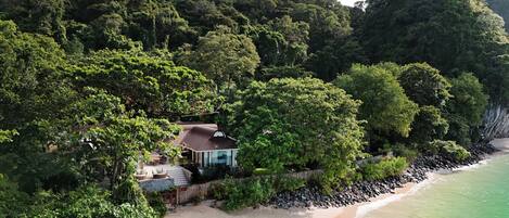 Una propiedad costera con una casa rodeada de un bosque denso, una playa arenosa y un litoral rocoso.