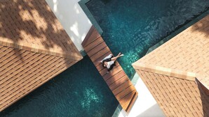 Una persona en una cubierta de madera sobre una piscina con agua cristalina, rodeada de paredes con azulejos y un techo blanco.