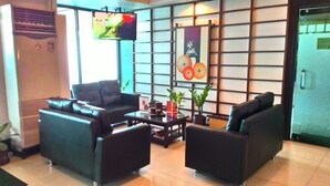 Un espace d’accueil avec des canapés en cuir noir, une table basse et un téléviseur fixé au mur.