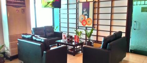 Un área de recepción con sofás de cuero negro, una mesa de centro y un televisor montado en la pared.