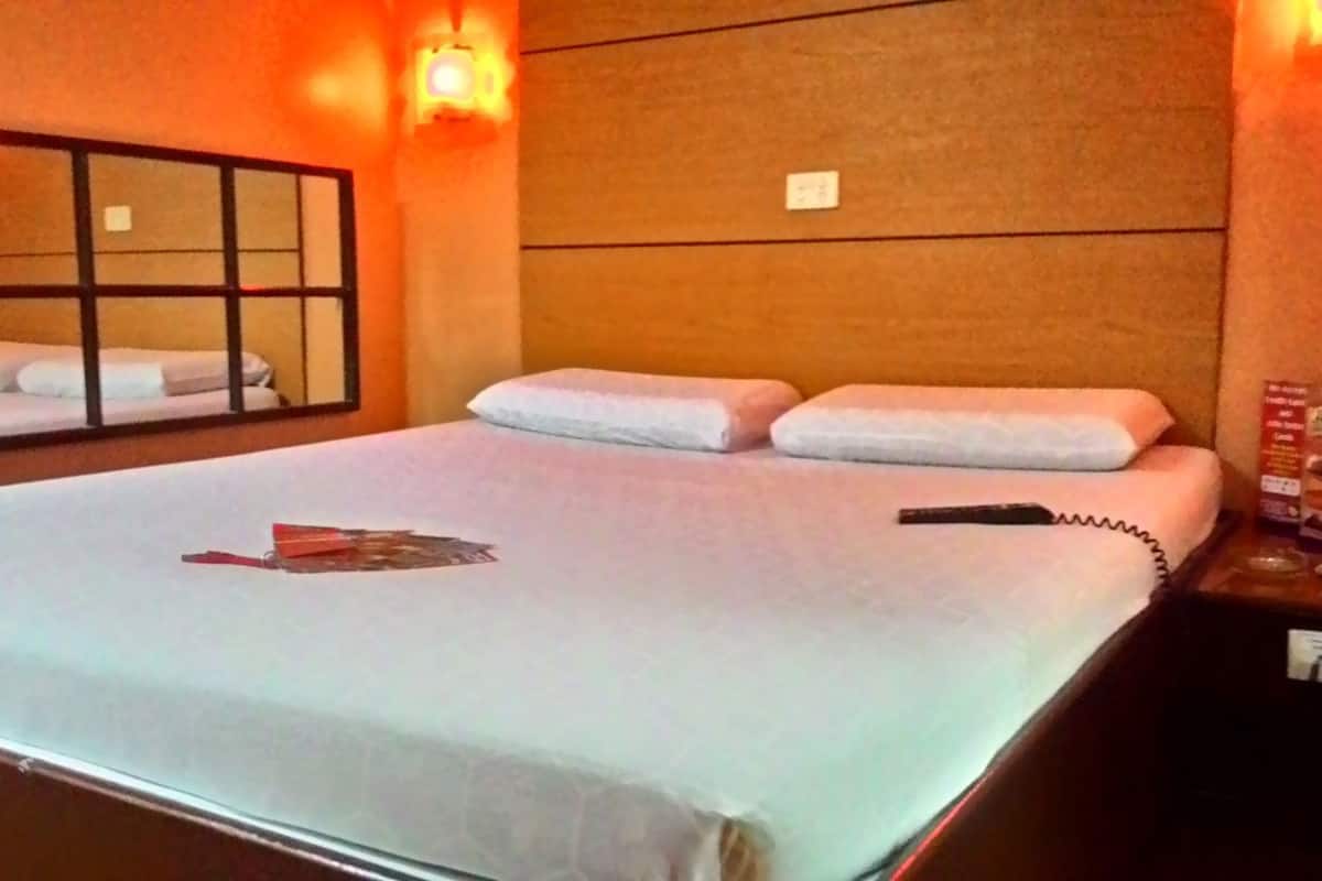 Een hotelkamer met een groot bed, een nachtkastje met een afstandsbediening en een spiegel aan de muur.