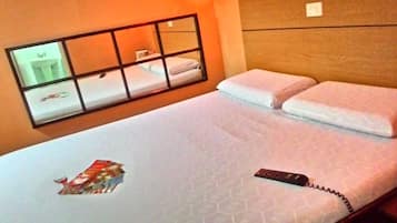 Una habitación de hotel con una cama, un ventanal con vistas a un lavamanos y un espejo, y un control remoto sobre la cama.