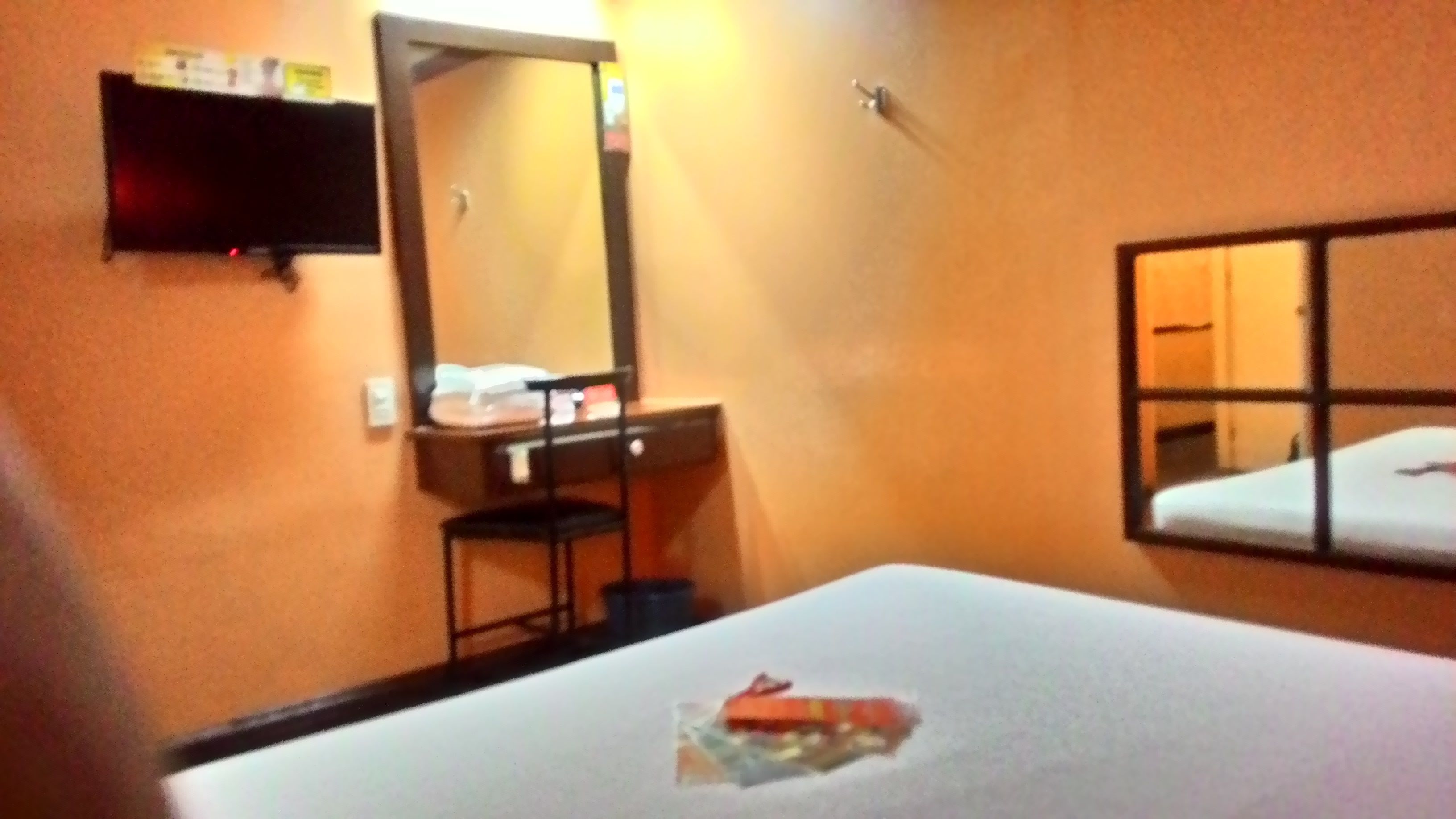 Ein Hotelzimmer mit Bett, Schreibtisch mit Stuhl, Spiegel und Ablagefläche mit Gegenständen.