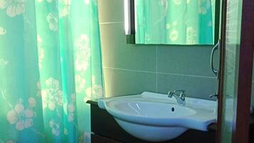 Un baño con lavamanos, espejo y cortinas con motivos florales.