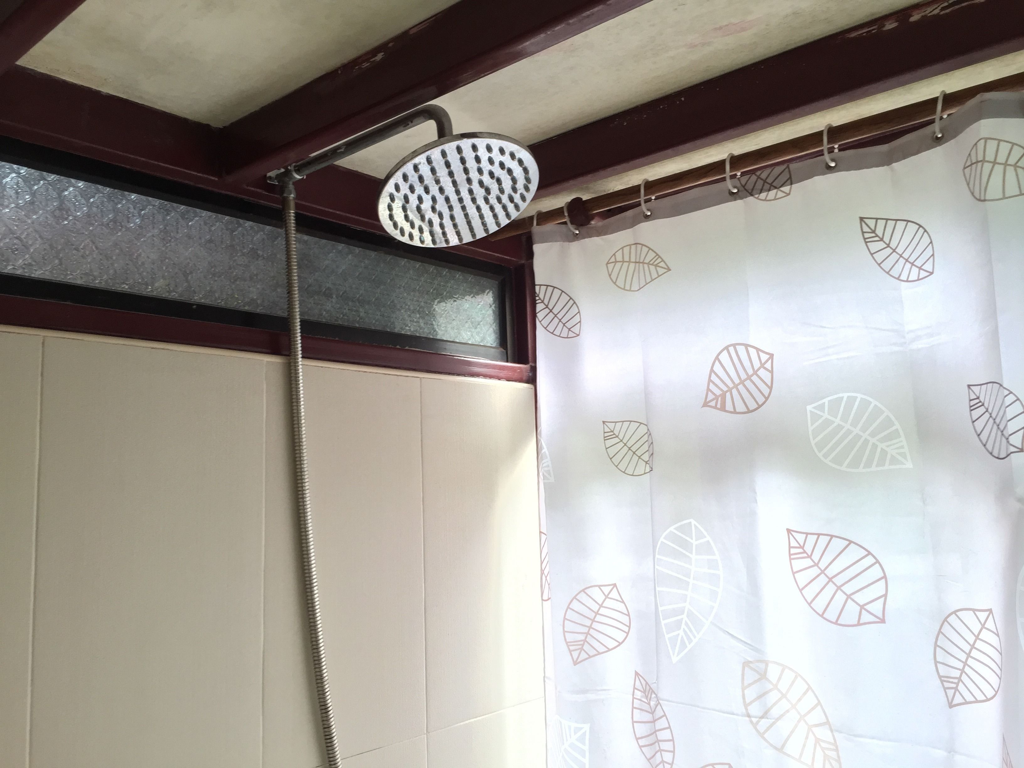Ducha con cabezal de ducha de mano y cortina con estampado de hojas.