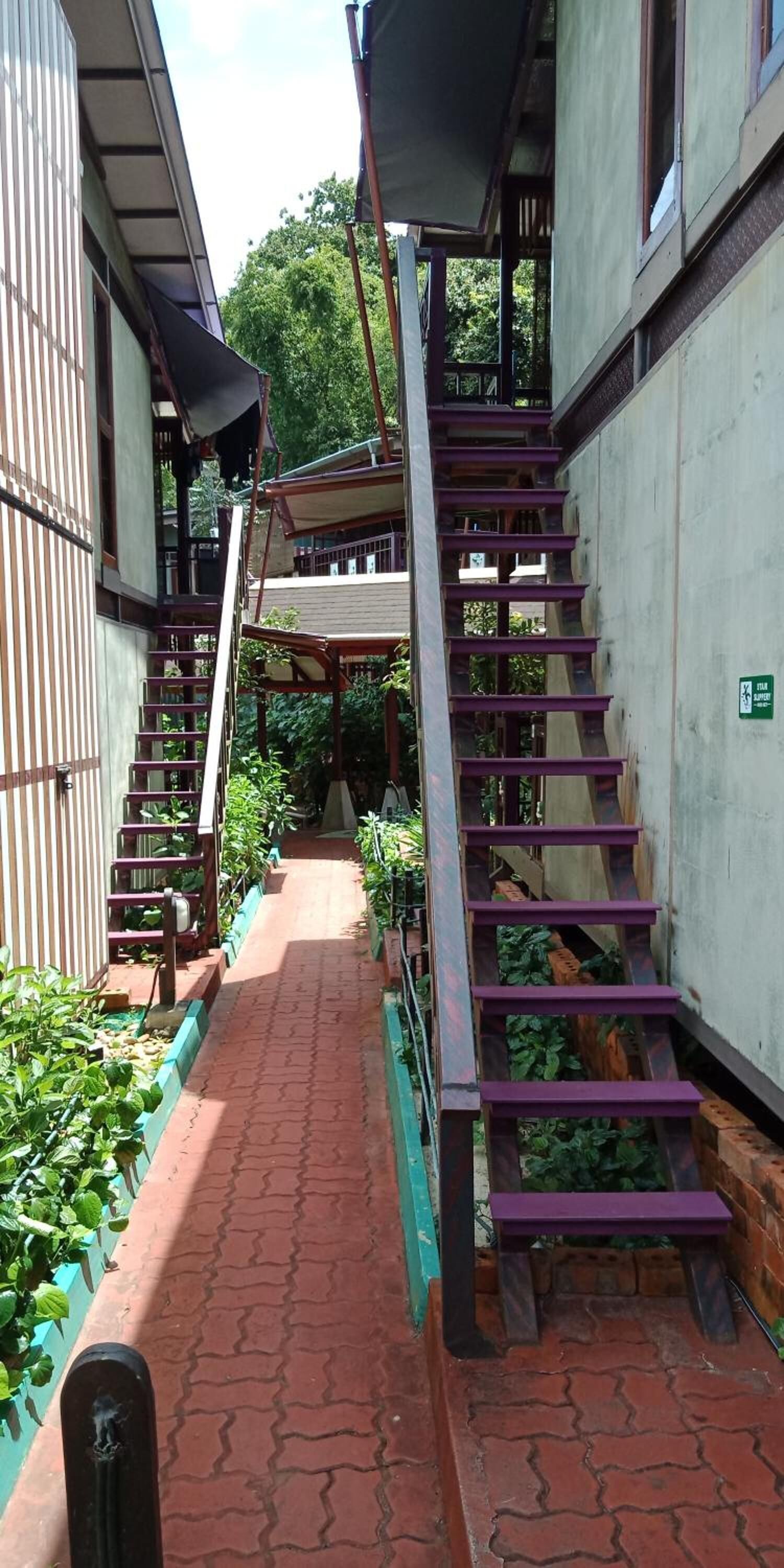 Escadaria externa estreita com guarda-corpo roxo, que dá acesso a uma área coberta.