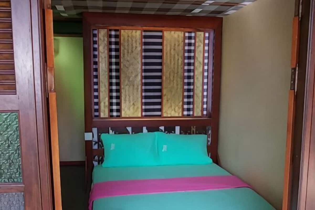 A room with a bed, a wooden headboard, and a window with vertical blinds.