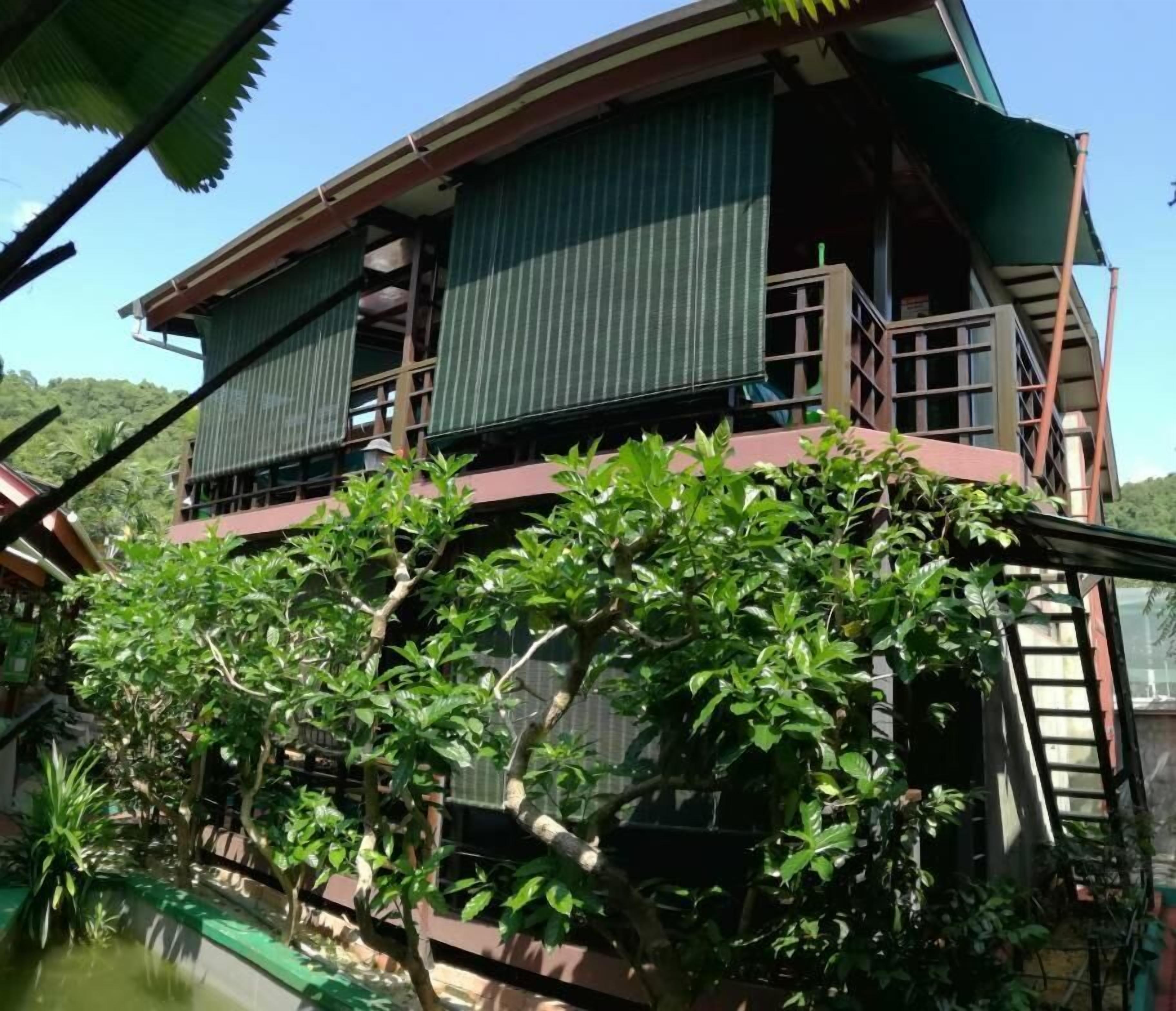 A two-story building with a balcony on the upper floor, surrounded by greenery.