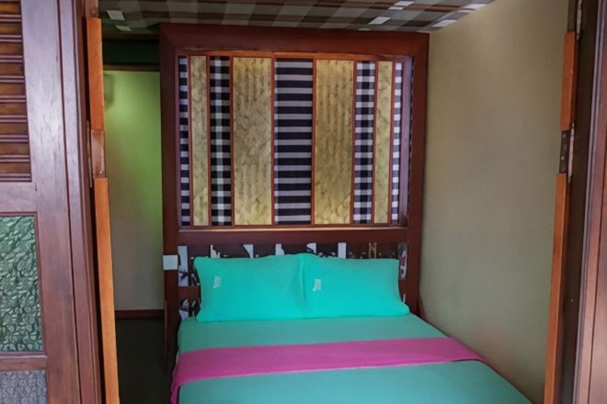 Une chambre avec un lit, une tête de lit en bois et une fenêtre avec des stores verticaux.