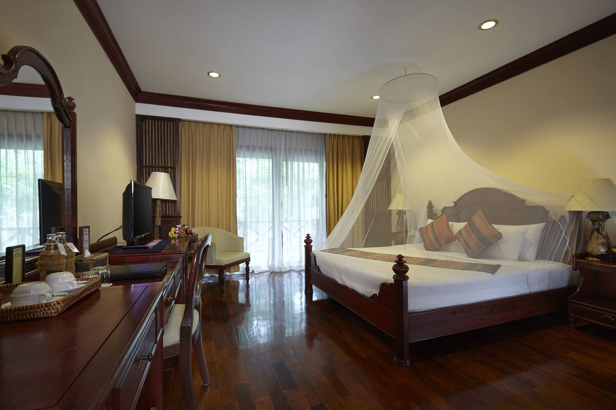 A hotel room with a wooden bed, a television, a desk with a lamp, and a chair.