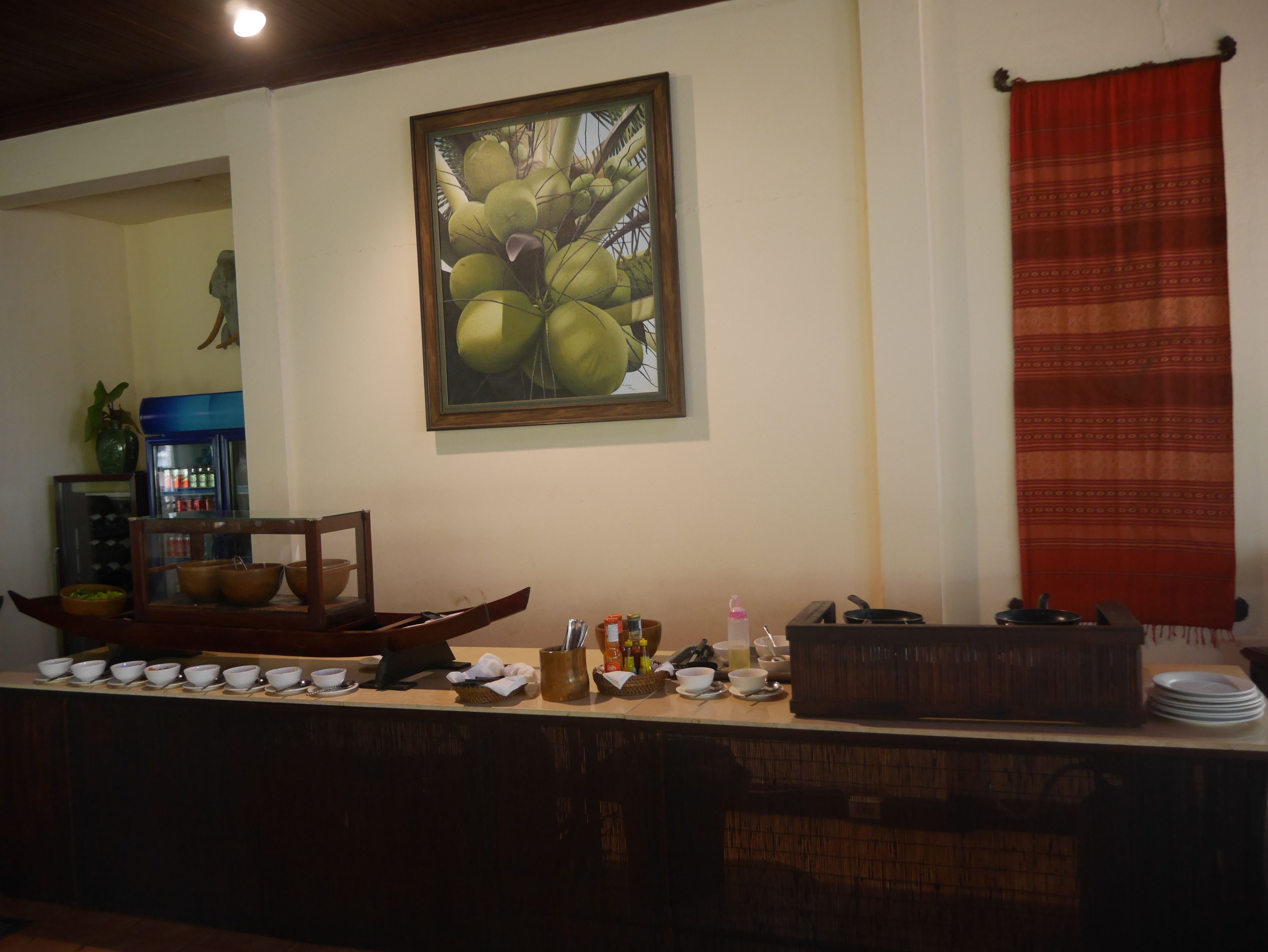 Una cocina con mostrador que exhibe varios cuencos, un cuadro de cocos, un refrigerador y una cortina roja.