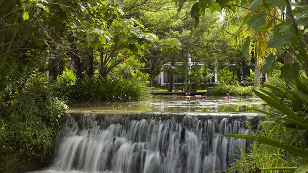 A waterfall surrounded by lush greenery and a small pond with pink flowers. - Santi Resort & Spa (Luang Prabang)