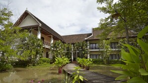 A traditional wooden house with a wooden deck over a pond, surrounded by lush greenery. - Santi Resort & Spa (Luang Prabang)