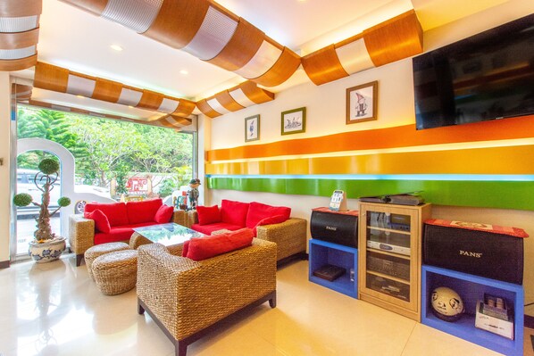 Um saguão de hotel com móveis de vime, um sofá vermelho, uma televisão e uma parede verde.