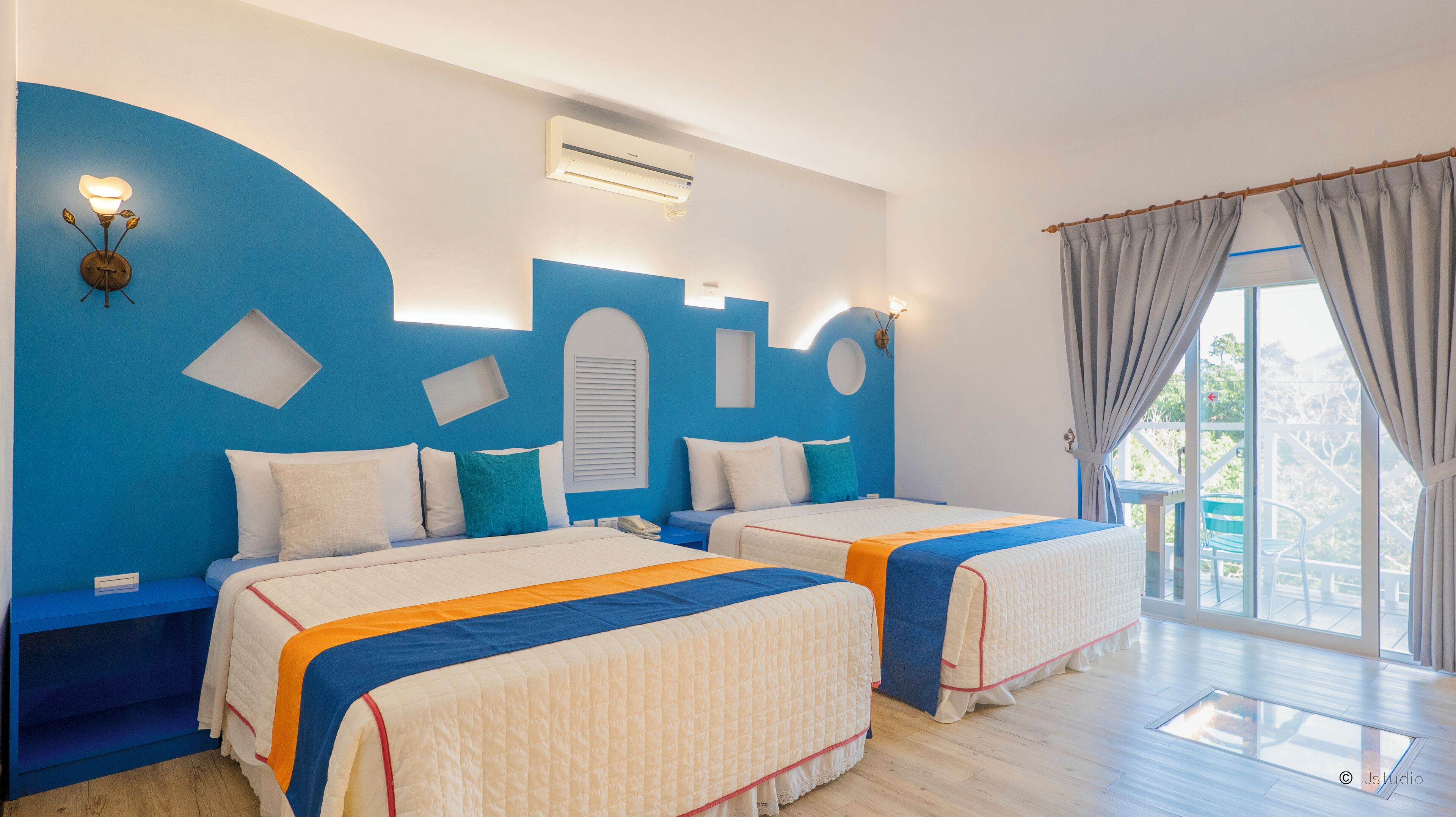 Habitación de hotel con dos camas, una pared de acento azul, una ventana con cortinas y vistas a zonas verdes.