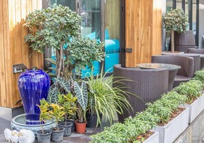 A patio area with wicker furniture, potted plants, and a blue decorative fountain. - The Bed Hatyai (Hat Yai)