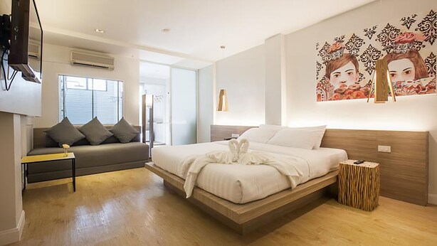 A modern bedroom with a bed, a sofa, a TV, and a painting on the wall. - The Bed Hatyai (Hat Yai)