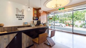 A reception desk with a sign for Martin Wales Inn, a wooden reception desk, a chandelier, and a view of the street outside. - Martin Wales Hotel Kenting (Hengchun)