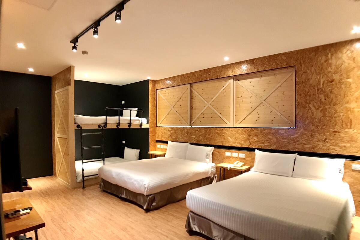 A hotel room with two beds, a wooden accent wall, and a bunk bed in the corner.