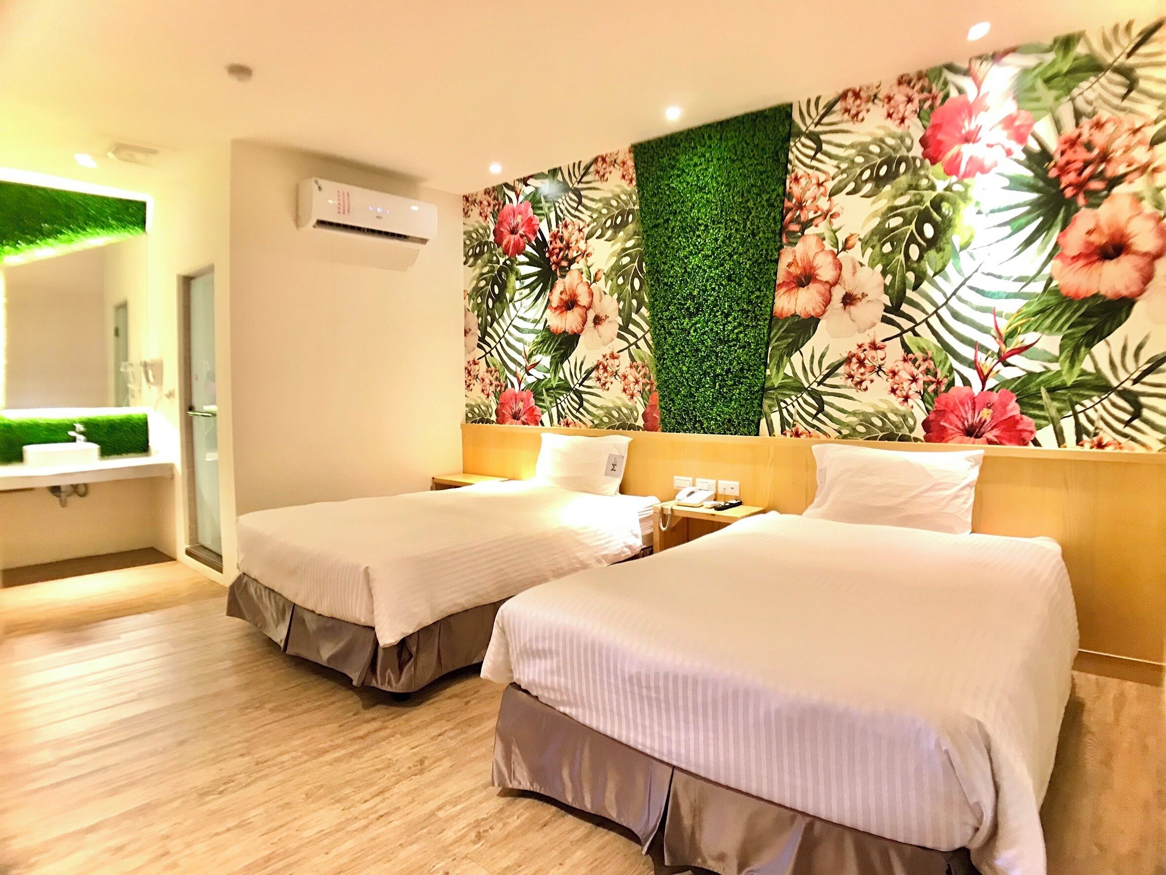 A hotel room with two beds, a bathroom with a mirror, and a wall decorated with floral wallpaper. - Martin Wales Hotel Kenting (Hengchun)