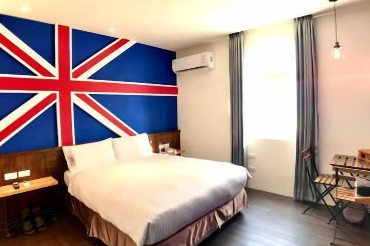 A hotel room with a large flag on the wall, a bed, a desk, and a chair.