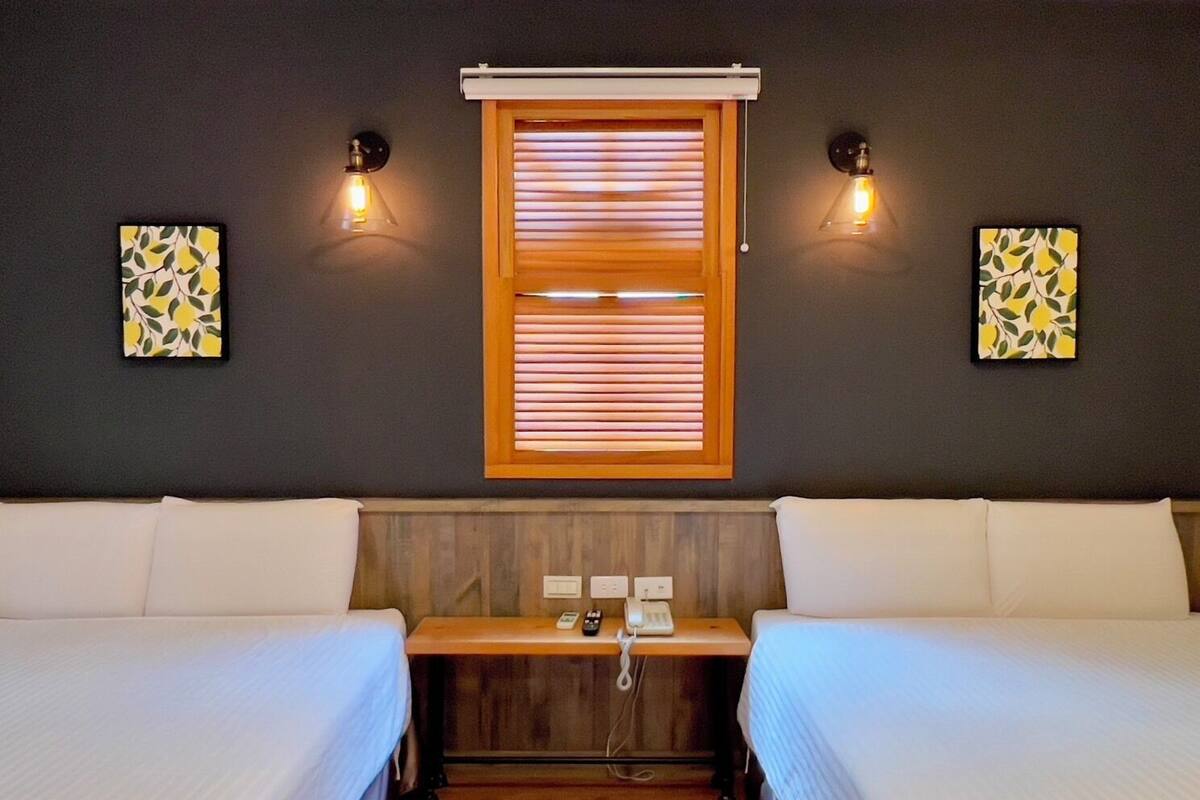 A room with two beds, a wooden bench, a telephone, and wall-mounted light fixtures.