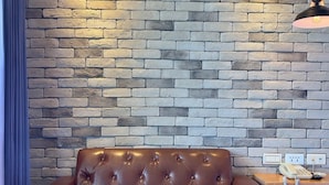 A brown leather sofa, a wooden table with a 'M' logo, and a brick wall with a hanging light fixture. - Martin Wales Hotel Kenting (Hengchun)