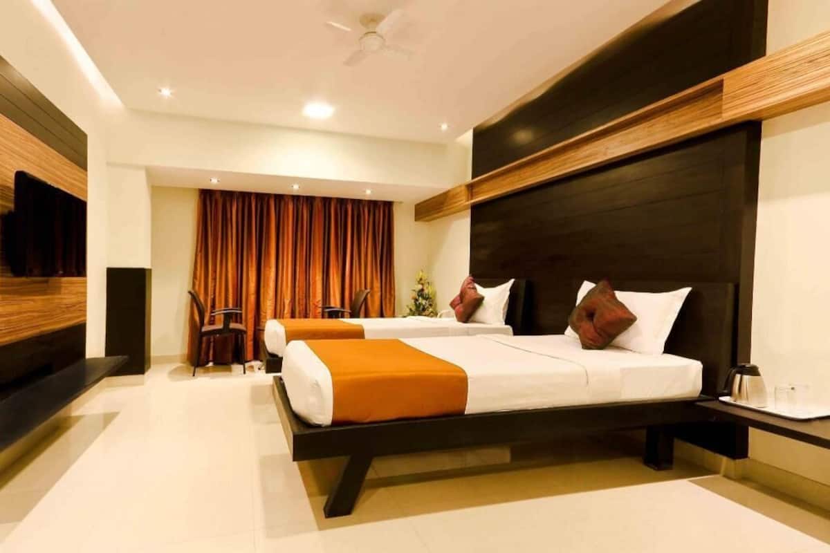A hotel room with two beds, a TV, a desk with a chair, and a large window with curtains.