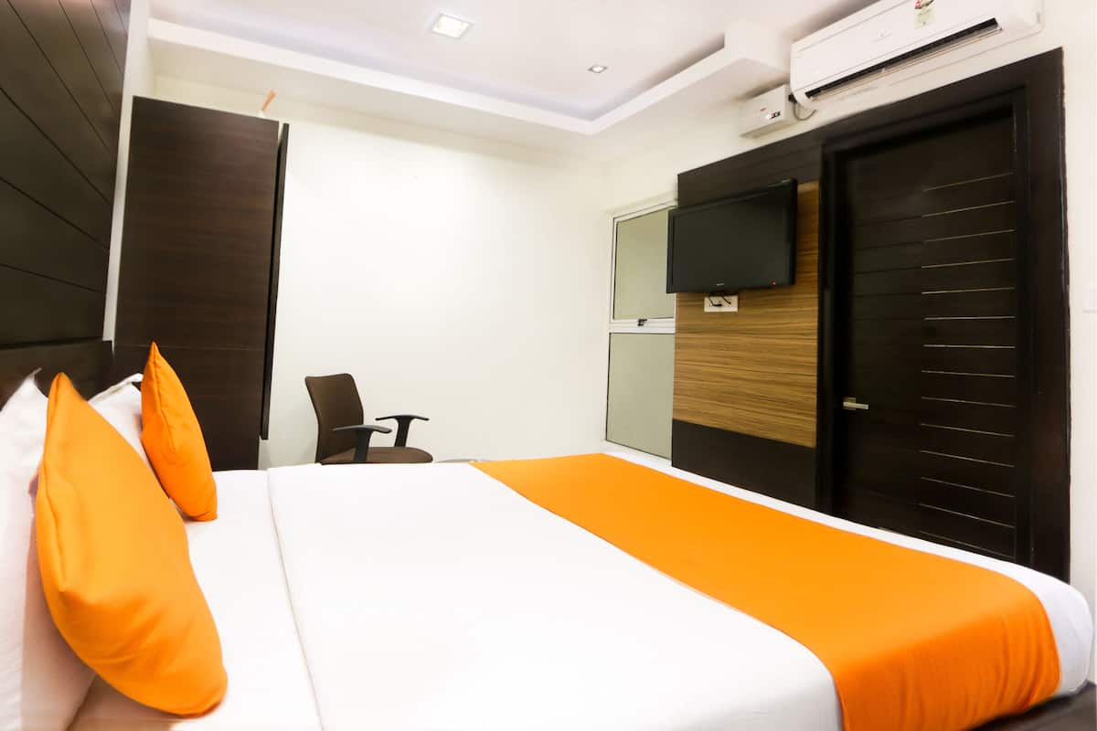 A hotel room with a bed, a chair, a television, and an air conditioning unit.
