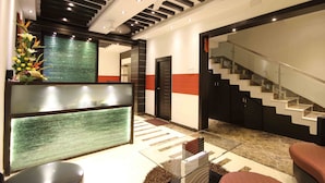 Un espace d’accueil moderne avec un bureau en verre, une plante décorative, un escalier et un miroir fixé au mur.